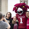 A division staff member takes a photo of a student and their parent with the Temple mascot, Hooter. 